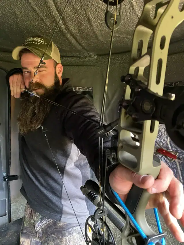 Man drawing his bow inside a hunting blind