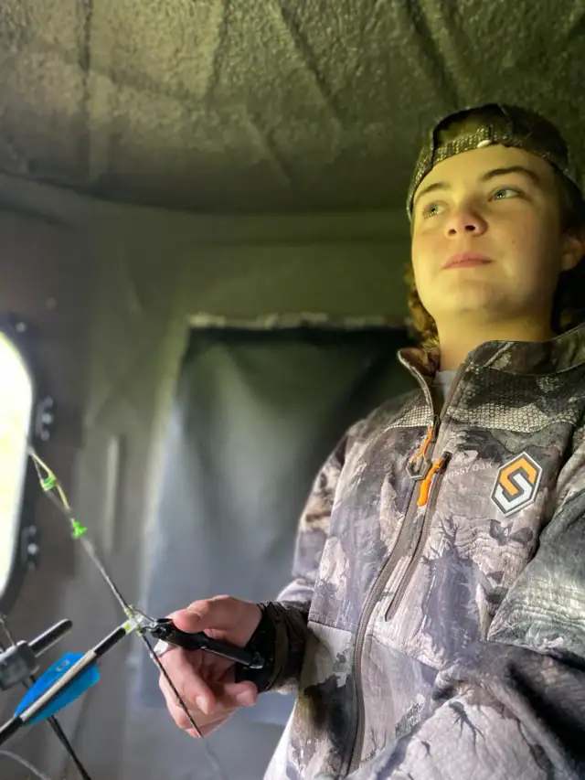 Teen holding bow inside a deer blind