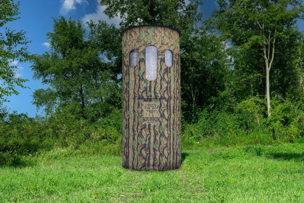 The Ultimate Blind with combo windows set at the corner of a grassy field with woods behind it